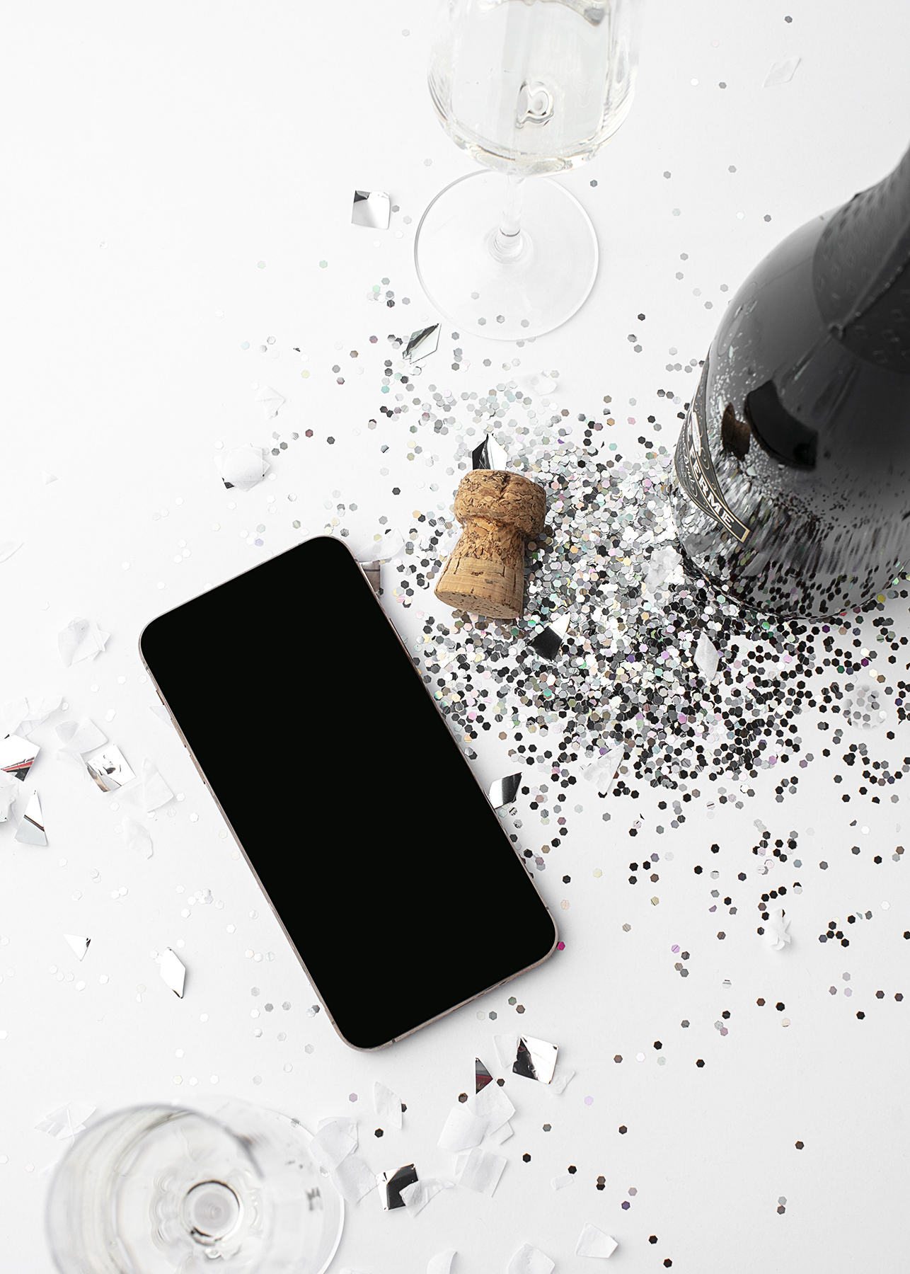 Picture of a phone with sparcles and an open champaigne bottle at a white desk